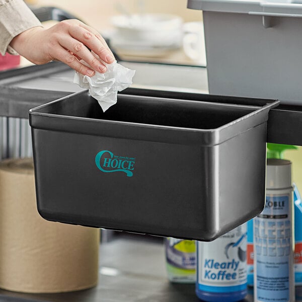 A person holding a plastic bag in a black Choice refuse bin for a cart.