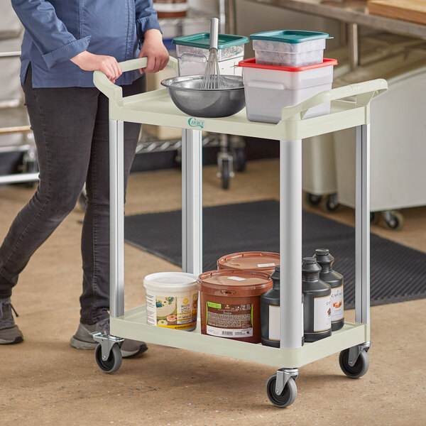 A woman using a Choice beige utility cart to transport containers and buckets.