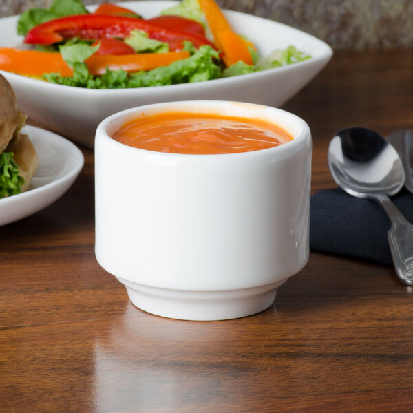 A Homer Laughlin bright white china bowl filled with soup on a table with a sandwich and salad.
