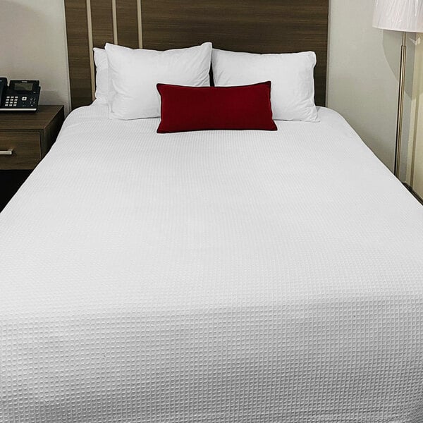 A bed with a white Oxford Jaipur thermal blanket and a red pillow.