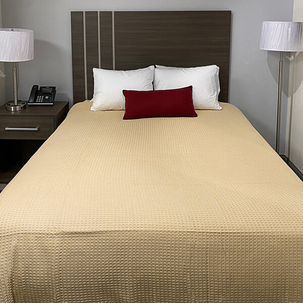 A bed with a tan Oxford Jaipur thermal honeycomb blanket and pillows in a hotel room.