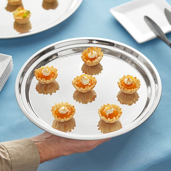 A person's arm holding an Acopa stainless steel catering tray with small appetizers.