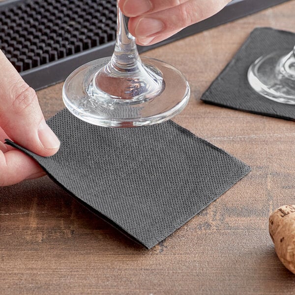 A person using a Hoffmaster FashnPoint black beverage napkin to hold a wine glass while pouring.