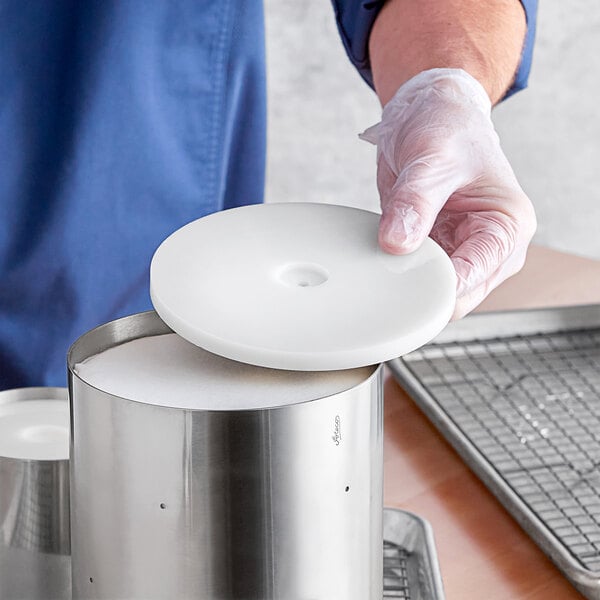 A person wearing gloves holding a white disc with a circular design.