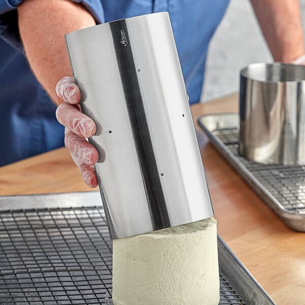 A person using a Ateco stainless steel round cheese mold to make a cheese round.