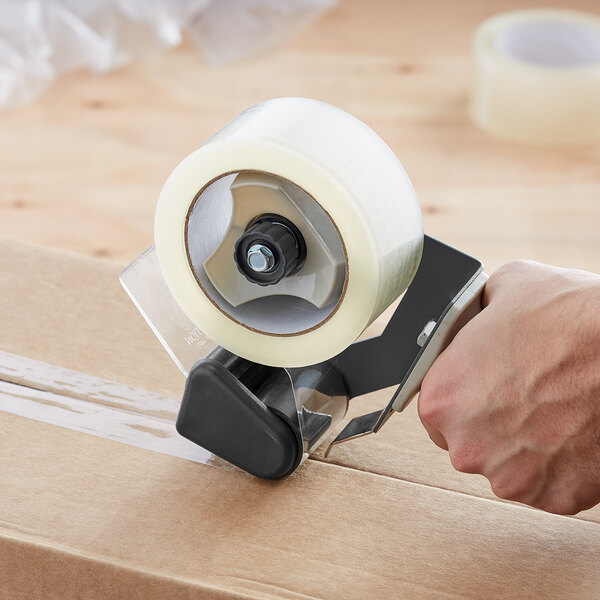 A hand using a tape dispenser to seal a box.