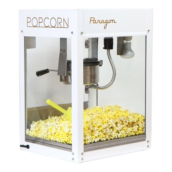 A white popcorn machine filled with freshly popped popcorn and a yellow scoop inside.
