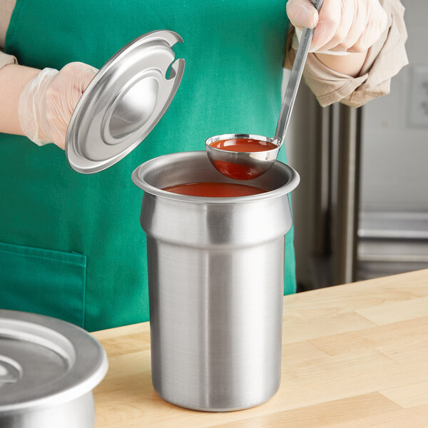 A woman using a Jacob's Pride ladle to pour sauce into a Vollrath stainless steel container.