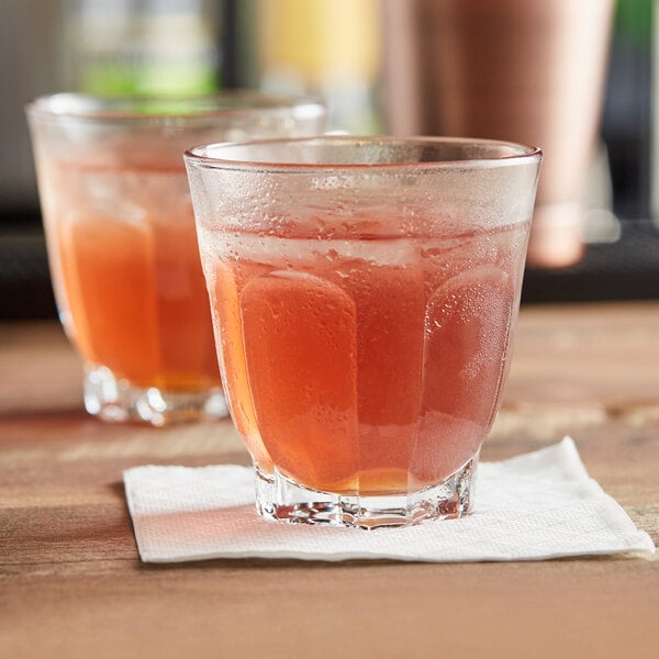 Two Arcoroc Arcadie rocks glasses filled with a red drink on a table.