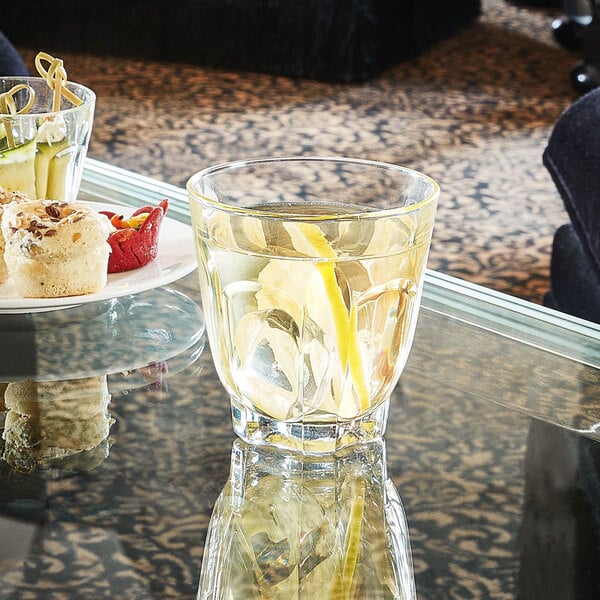 An Arcoroc old fashioned glass filled with water and ice with a lemon wedge on a table.