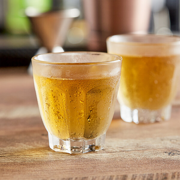 Two Arcoroc Arcadie Rocks glasses filled with a brown liquid on a table.