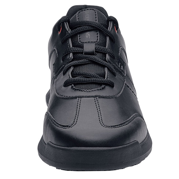 A black Shoes For Crews athletic shoe with red accents and laces.