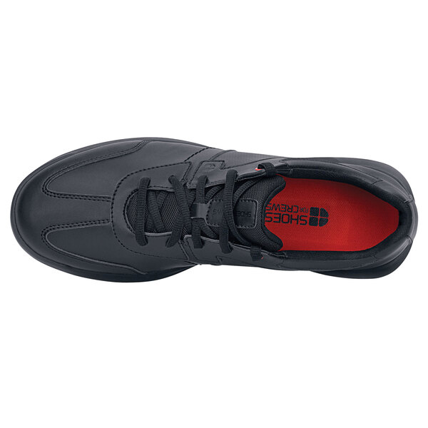 A black Shoes For Crews athletic shoe with a red sole.