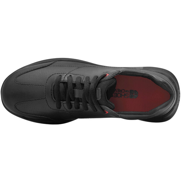 A black leather Shoes For Crews women's athletic shoe with a red sole on a table.