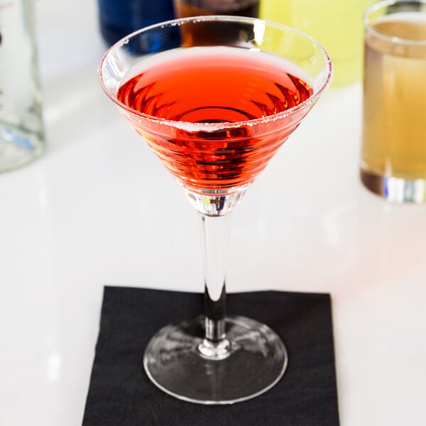 A martini glass with a red cocktail on a table in a cocktail bar.