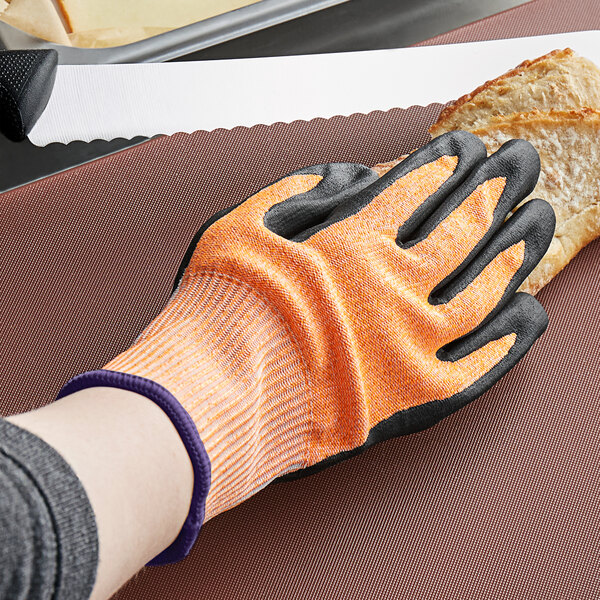 A hand wearing an orange and white Mercer Culinary Millennia food processing glove cuts a piece of bread.