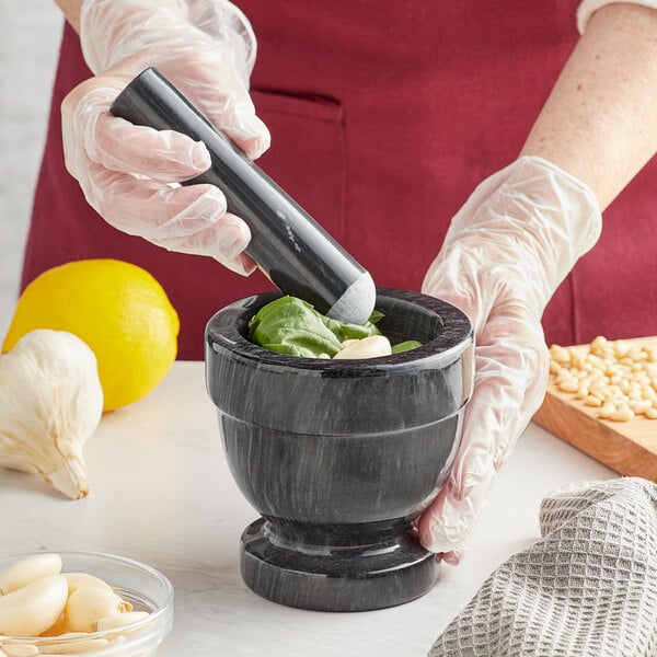A person in gloves grinding basil and garlic in a Fox Run black marble mortar.