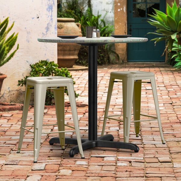 A Lancaster Table & Seating Excalibur outdoor table base with stools on a brick patio.