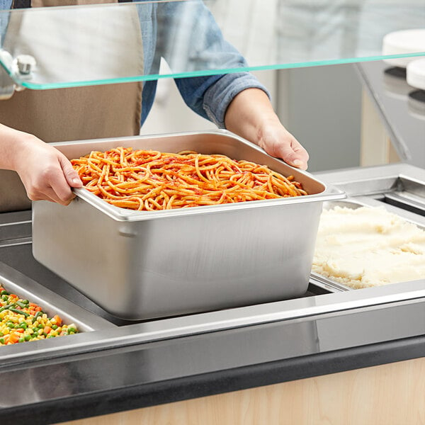 A person using a Vigor stainless steel steam table pan to serve food.