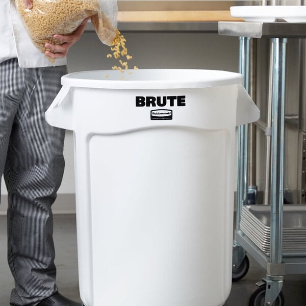 A man pouring food into a large white Rubbermaid ingredient storage bin.