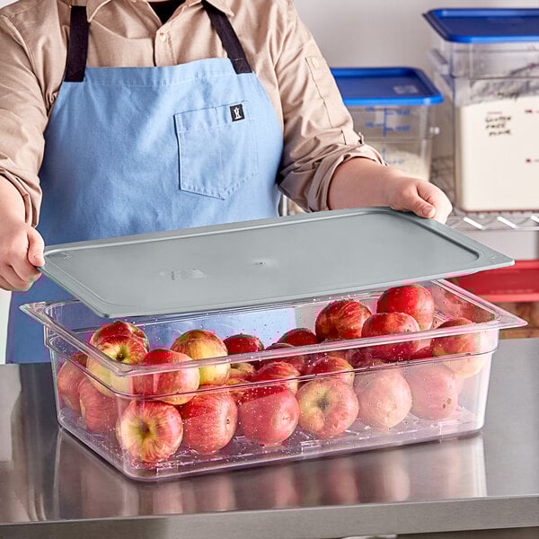 A man in an apron holding a Vigor clear food pan with a tray of apples.
