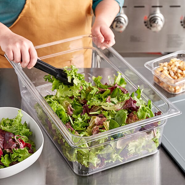 A woman using a Vigor clear plastic food pan to hold salad at a salad bar.