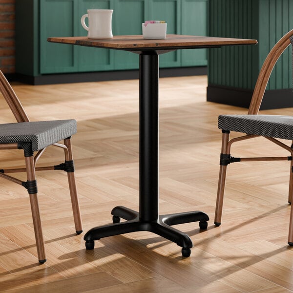 A black metal outdoor table base with a cross-shaped bottom and a standard height column, supporting a square tabletop.