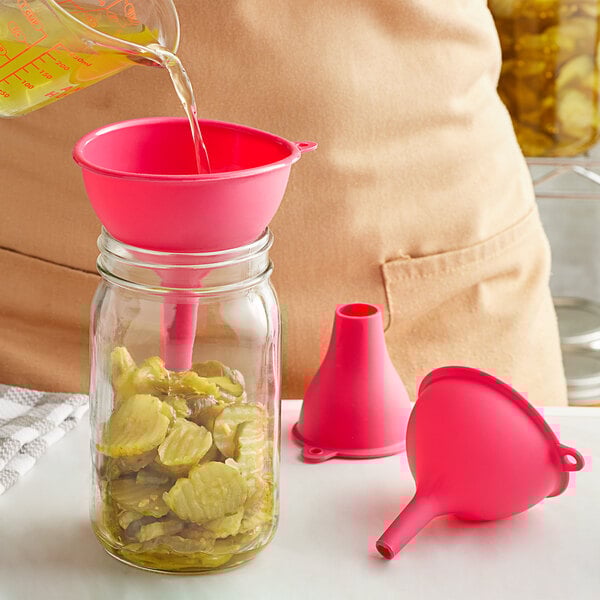 A person using a pink Fox Run silicone funnel to pour liquid into a jar.