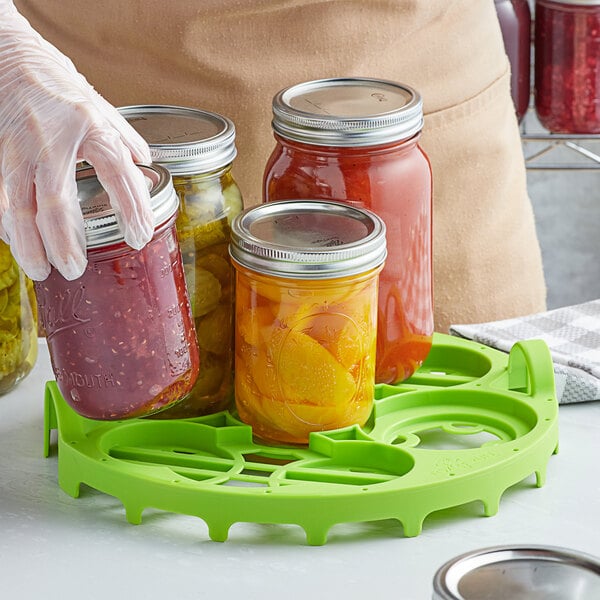 A person using a Fox Run green nylon canning rack to hold jars of food.