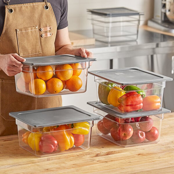 A man holding a Vigor 1/2 size clear food pan with a secure sealing cover containing oranges.