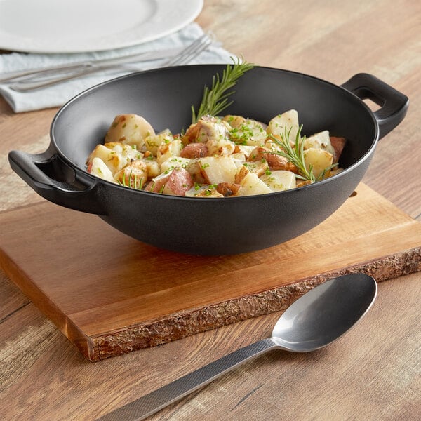 An American Metalcraft black faux cast iron serving bowl with food and herbs on a table.