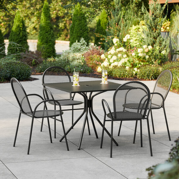 A Lancaster Table & Seating Harbor black table with four chairs on an outdoor patio.