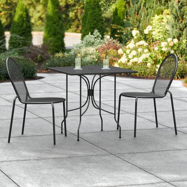 A Lancaster Table & Seating black outdoor table with two chairs on a patio.