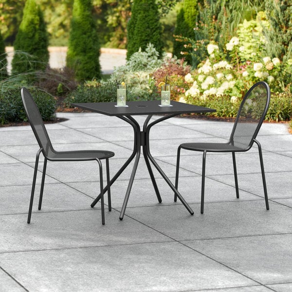 A Lancaster Table & Seating Harbor outdoor table with black chairs on a patio.