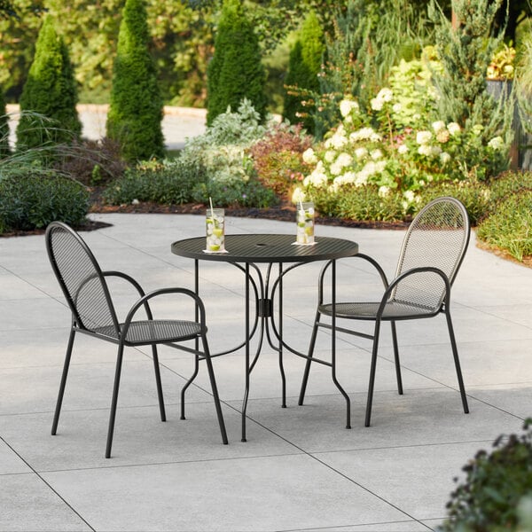 A Lancaster Table & Seating Harbor black round table with two arm chairs on an outdoor patio.