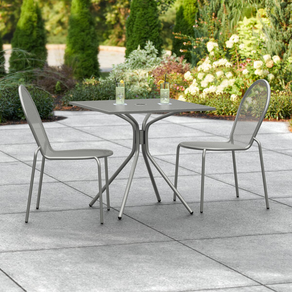 A Lancaster Table & Seating Harbor Gray outdoor table with two chairs on a patio.