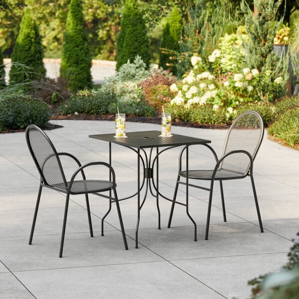 A Lancaster Table & Seating Harbor black rectangular outdoor table with ornate legs and two arm chairs on a patio.