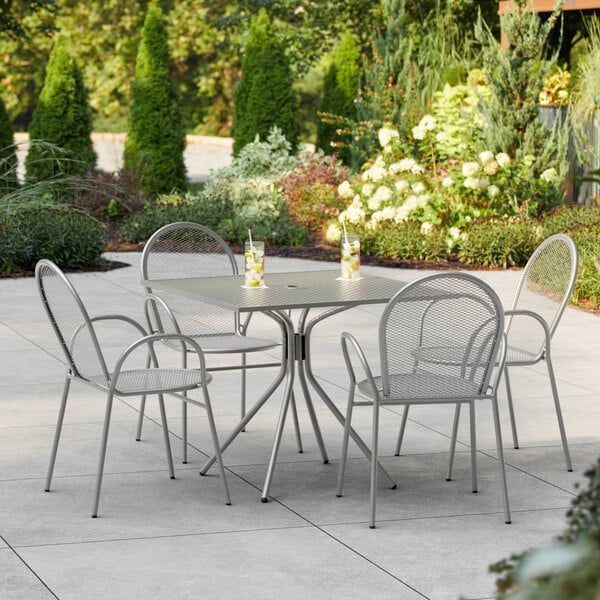 A Lancaster Table & Seating Harbor Gray table with four arm chairs on an outdoor patio.