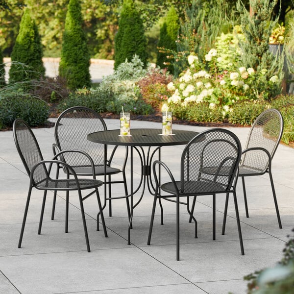 A Lancaster Table & Seating black outdoor table with ornate legs and four arm chairs on a patio.