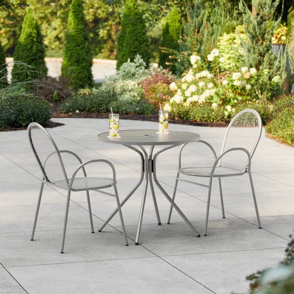 A Lancaster Table & Seating Harbor Gray table and chairs on an outdoor patio with two cups on the table.
