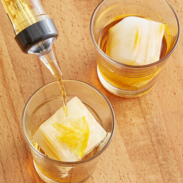 A glass of liquid being poured into a glass of ice cubes made with Choice Black Silicone 2" Cube Ice Mold.