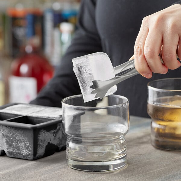 A person using tongs to place a Choice Black Silicone 2" cube ice into a glass.