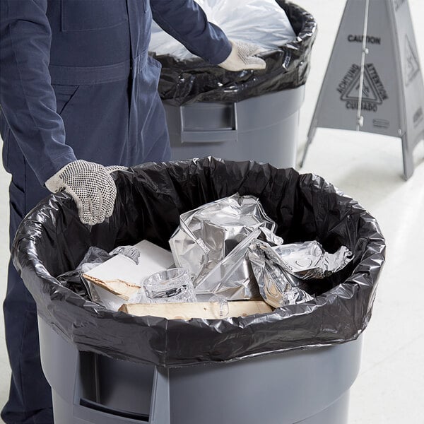 A man in a blue coverall holding a black Lavex Hercules trash bag.