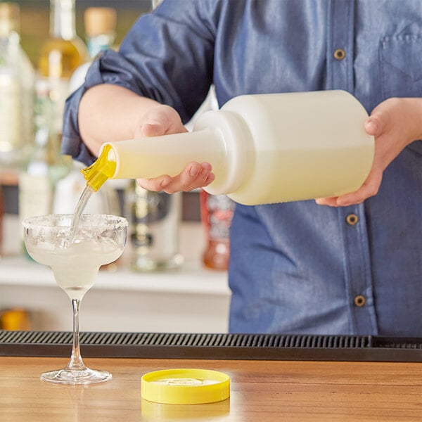 A person pouring a drink from a Choice white pour bottle with yellow lid and spout into a glass.