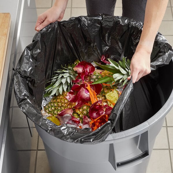 A woman putting fruit in a Lavex trash bag.