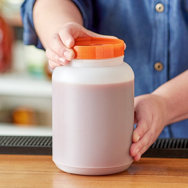 A person holding a Choice plastic container with orange cap filled with brown liquid.