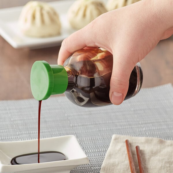 A hand pouring Town Round Green Top Soy Sauce into a white bowl of dumplings.