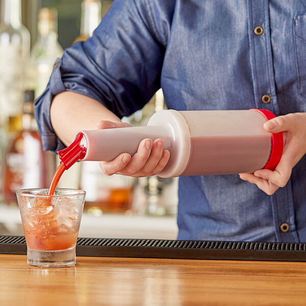 A person using a Choice plastic pour bottle with red cap to pour a pink cocktail into a glass with a straw.