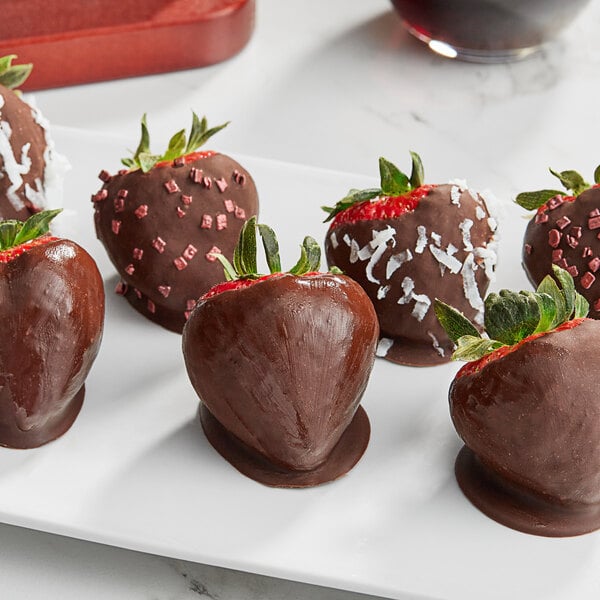 A plate of chocolate covered strawberries with coconut and squares on one.