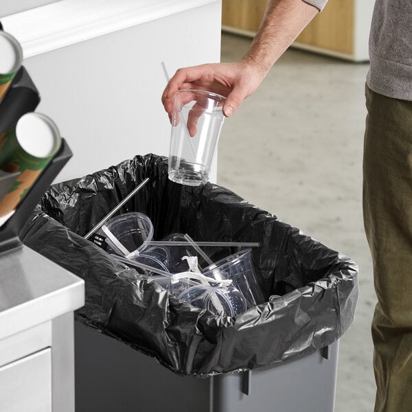 A man putting a plastic cup into a Lavex Li'l Herc trash bag in a trash can.